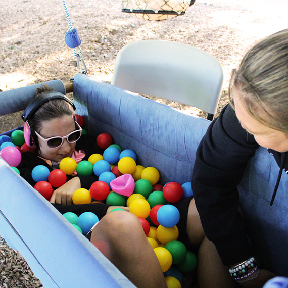 Participant in swing surrounded by ball pit balls with mentor.