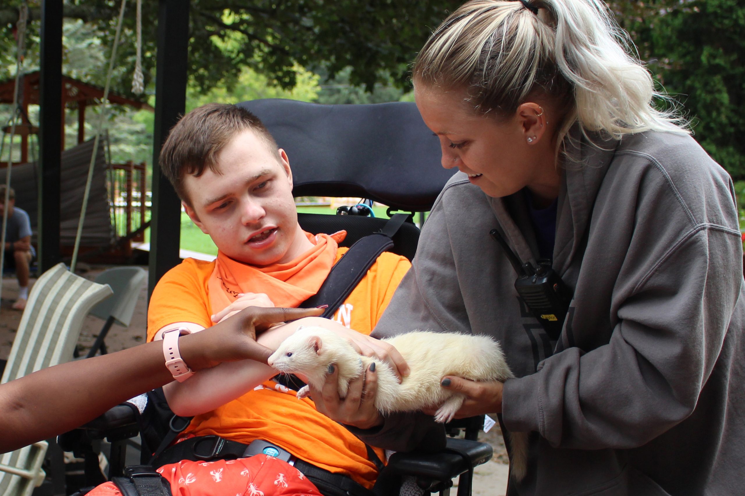 Participant smiling while interacting with a white ferret alongside an Animal Care Team member.